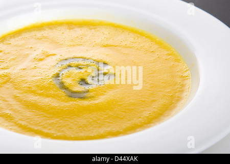 Schüssel mit Karotten und Koriander golden gefärbt Suppe mit grünen Kraut Garnitur in weiß Schüssel ruhen auf weißen Teller serviert Stockfoto