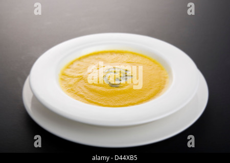 Schüssel mit Karotten und Koriander golden gefärbt Suppe mit grünen Kraut Garnitur in weiß Schüssel ruhen auf weißen Teller serviert Stockfoto