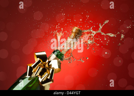 Knallende Korken aus Champagner-Flasche mit viel Spritzer rot Hintergrund Stockfoto