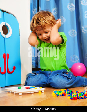 Zwei Jahre alten Jungen spielen und lachen, sitzen auf dem Boden in seinem Zimmer mit Mosaik Stockfoto