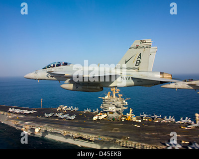 Zwei F/A-18-Kampfflugzeuge fliegen in Formation über die USS Enterprise im Arabischen Meer und demonstrieren während einer militärischen Operation die Fähigkeiten der Marine. Stockfoto