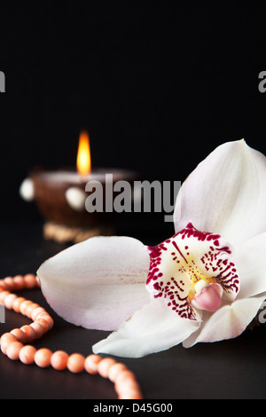 Orchidee Blume, Korallen Perlen und eine brennende Kerze auf einem schwarzen Hintergrund Stockfoto