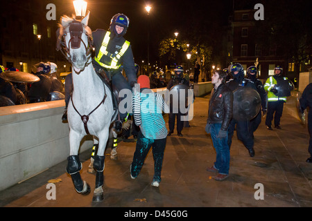 Polizisten in voller Kampfausrüstung ziehen eine protestierende Studenten durch seine Kleider auf Whitehall bei Nacht, Tag X3 montiert Studentendemonstration, London, England Stockfoto