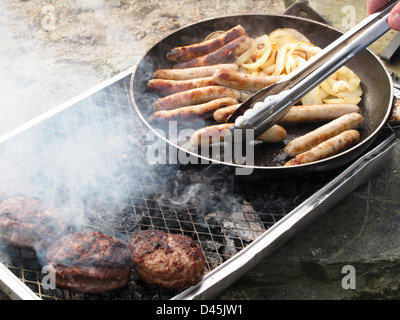 Würstchen und Zwiebeln auf Einweg-Grill und Hacksteaks Grillen Braten Stockfoto