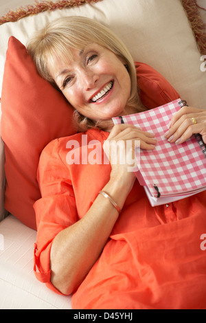 Senior Woman Sitting On Sofa lesen Tagebuch Stockfoto