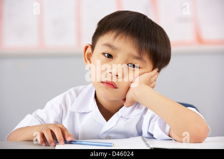 Unglückliche männlichen Studenten, die Arbeiten am Schreibtisch In Chinesisch Schule Unterricht Stockfoto