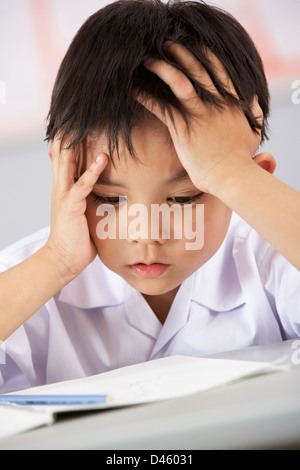 Unglückliche männlichen Studenten, die Arbeiten am Schreibtisch In Chinesisch Schule Unterricht Stockfoto