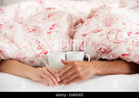 Romantisches Paar Hand in Hand unter der Bettdecke im Bett Stockfoto