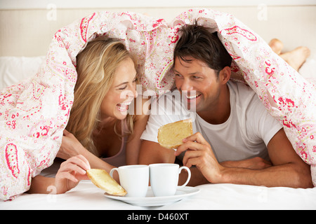 Paar kuschelte sich unter die Bettdecke zu frühstücken Stockfoto