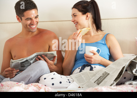 Paar frühstücken und Zeitung im Bett lesen Stockfoto