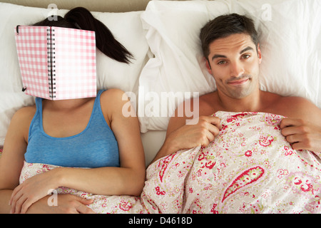 Langweilig aussehenden Mann im Bett neben Frau Lesebuch Stockfoto