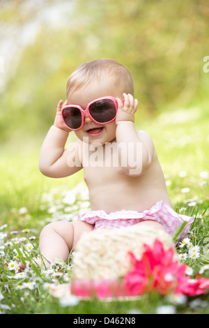 Babymädchen im Sommerkleid sitzt im Feld mit Sonnenbrille Stockfoto