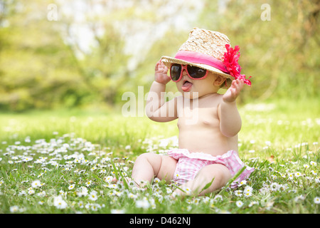 Babymädchen im Sommerkleid sitzen im Feld tragen Sonnenbrillen und Strohhut Stockfoto