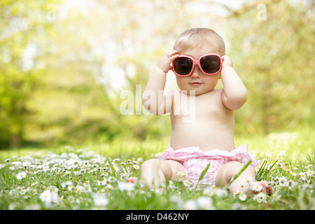 Babymädchen im Sommerkleid sitzt im Feld mit Sonnenbrille Stockfoto