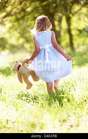 Junge Mädchen zu Fuß durch Sommerwiese mit Teddybär Stockfoto