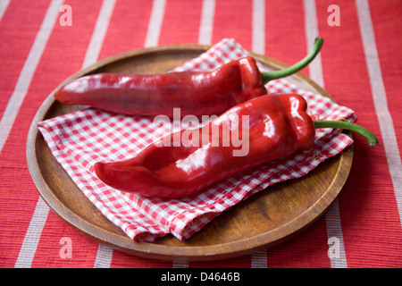 Zwei italienische Romano spitz Paprika nebeneinander auf einer Holzplatte mit einem roten Scheck Serviette und gestreifte Tischdecke. Stockfoto