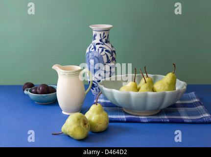 Koordinierte Stillleben von Geschirr, Birnen und Pflaumen auf a blaue Tabelle mit einem grünen Hintergrund Farbe Stockfoto