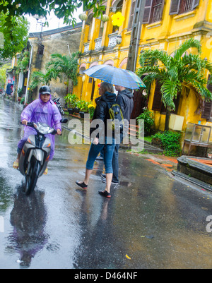 Touristen zu Fuß Regen in Hoi an Vietnam mit Motorrad vorbeifahren Stockfoto