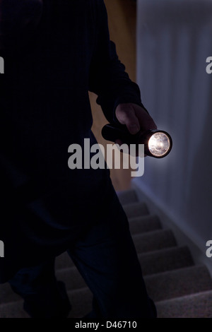 Schattenhafte männlichen Eindringling hält eine Fackel oder Taschenlampe Treppensteigen. Stockfoto