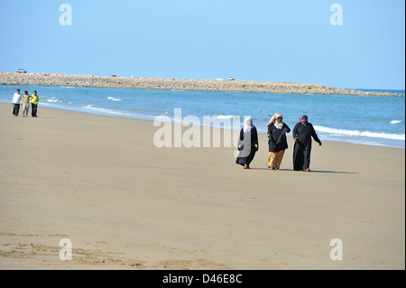 Drei muslimische Frauen schlendern Sie an den breiten Sandstrand am Yiti; Muscat, Oman. Stockfoto