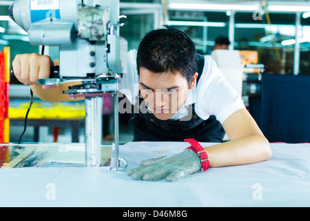 Arbeitnehmer mit einem Cutter - eine große Maschine für Schneiden Stoffe - in einer chinesischen Textilfabrik, He trägt angegossen Kette Stockfoto