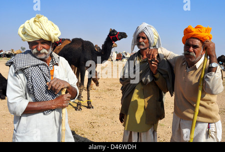 Kamel Händler lehnt sich auf ihrem Stick wie sie Uhren Kamele in der Nähe in einem Feld auf dem Kamel Messegelände in Nagaur, Staat Rajasthan. Stockfoto