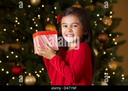 Mädchen hält Weihnachtsgeschenk vor Baum Stockfoto