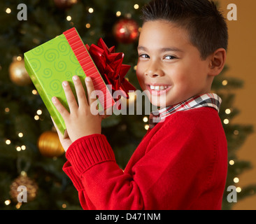 Junge hält Weihnachtsgeschenk vor Baum Stockfoto