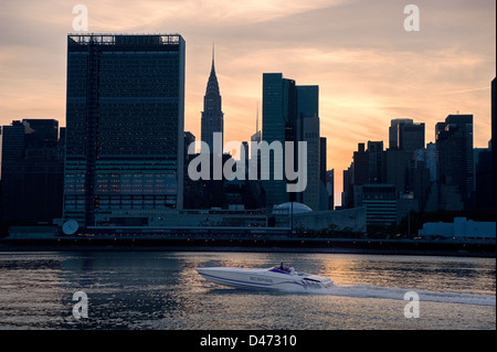 Ein Boot Geschwindigkeiten entlang des East River vor einer Silhouette Skyline New Yorks, UNO & Chrysler Gebäude. Stockfoto