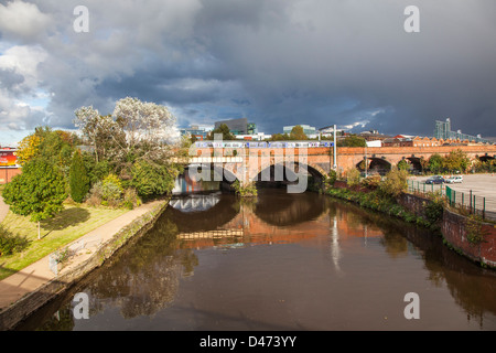 Manchester Ship Canal und Eisenbahnbrücke in der Nähe von Liverpool Street, Stadtteil Castlefield mit Spiegelbild im Wasser und stürmischen Himmel Stockfoto