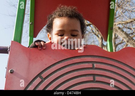 Gemischte Rassen Kleinkind Baby Lächeln und spielen am Klettergerüst an einem sonnigen Tag über Oberseite der Wand guckend Stockfoto