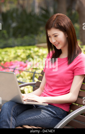 Junge Chinesin mit Laptop, während, entspannend auf Parkbank Stockfoto