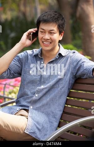 Junge chinesische Mann entspannend auf Parkbank telefonieren mit Handy Stockfoto