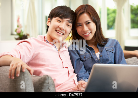 Junge chinesische paar mit Laptop, während Sie zu Hause auf Sofa entspannen Stockfoto