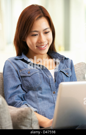 Junge Chinesin mit Laptop, während Sie zu Hause auf Sofa entspannen Stockfoto