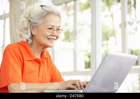 Hochrangige chinesische Frau sitzen am Schreibtisch mit Laptop zu Hause Stockfoto