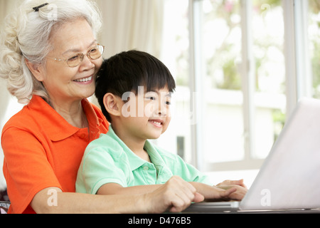 Chinesische Großmutter und Enkel sitzen am Schreibtisch mit Laptop zu Hause Stockfoto