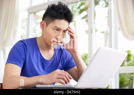 Jungen chinesische Mann am Schreibtisch mit Laptop zu Hause besorgt Stockfoto