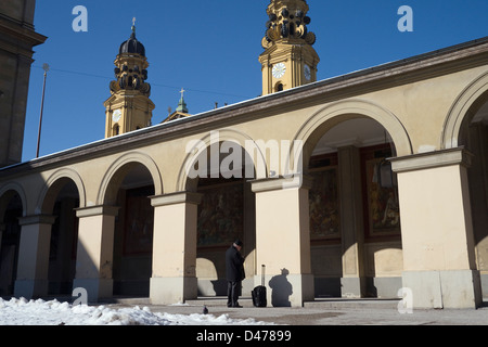 Mann mit Hut und Koffer mit Handy stand vor Torbogen und Gießen Schatten, München, Deutschland Stockfoto