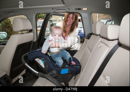 Reife Mutter, Baby Boy in seinem Autositz montiert und mit einem Gurt im hinteren Teil dieses Fahrzeug gesichert. Ältere Mutter Stockfoto