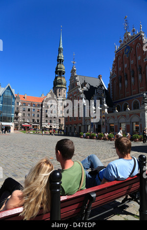 Touristen sitzen auf dem Rathausplatz (Ratslaukums), Blick auf Mitesser Haus und Turm der St. Peter Kirche Stockfoto