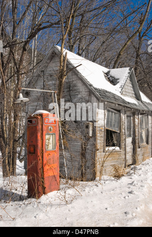 Eine verlassene alte altmodische eine Pumpe Tankstelle im Schnee und Sonne am Straßenrand. Stockfoto