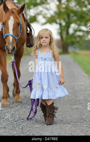 Blonde Mädchen ihr großes Pferd hinunter einen Sommer Feldweg führt. Stockfoto