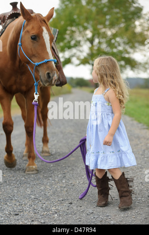 Kleine blonde Mädchen ihr großes Pferd auf einen Feldweg. Stockfoto