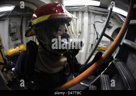 Ein Sailor übergibt während einer simulierten Feuerübung im Japanischen Meer einen Feuerschlauch an andere Seeleute und betont dabei die Schadenskontrolle und Notfallmaßnahmen an Bord eines Schiffes der US Navy. Stockfoto