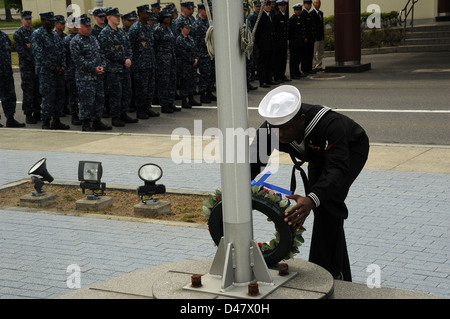 Ein Seemann, der Orte einen Kranz, gebildet von den roten, weißen und blauen Blumen, an der Basis von einem Fahnenmast in einem Moment der Stille am Naval Air facility Misawa Schlacht um Midway Gedenkveranstaltungen. Stockfoto