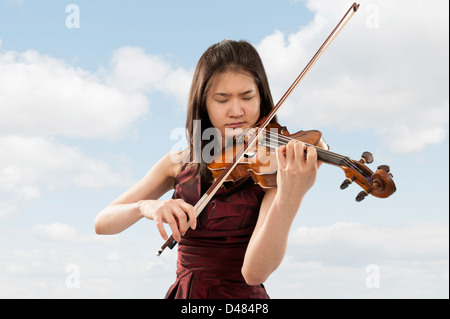 junge weibliche asiatische Geigenspieler auf Wolken-Hintergrund Stockfoto