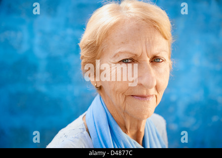 Ältere Leute Porträt, glückliche alte blonde Frau in Blu Kleidung lächelnd und Blick in die Kamera gegen blaue Wand Stockfoto