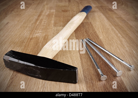 Hammer mit drei Nägeln auf einer Holzplatte. Stockfoto