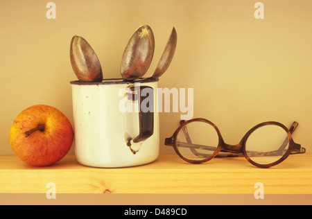 Augenhöhe Blick auf schmalen Holzregal mit Apple Emaille Becher mit drei Teelöffel und Vintage Brille Stockfoto